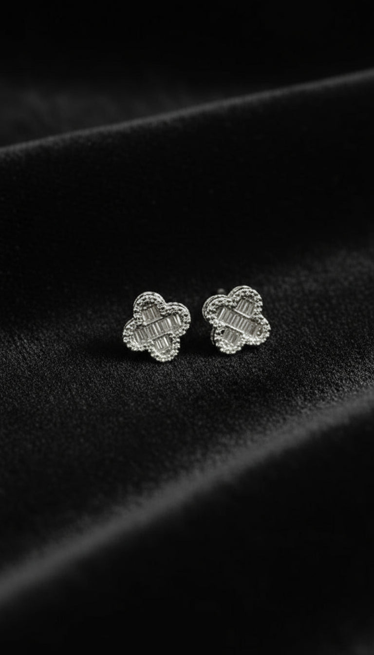 Silver clover-shaped earrings on a dark fabric background