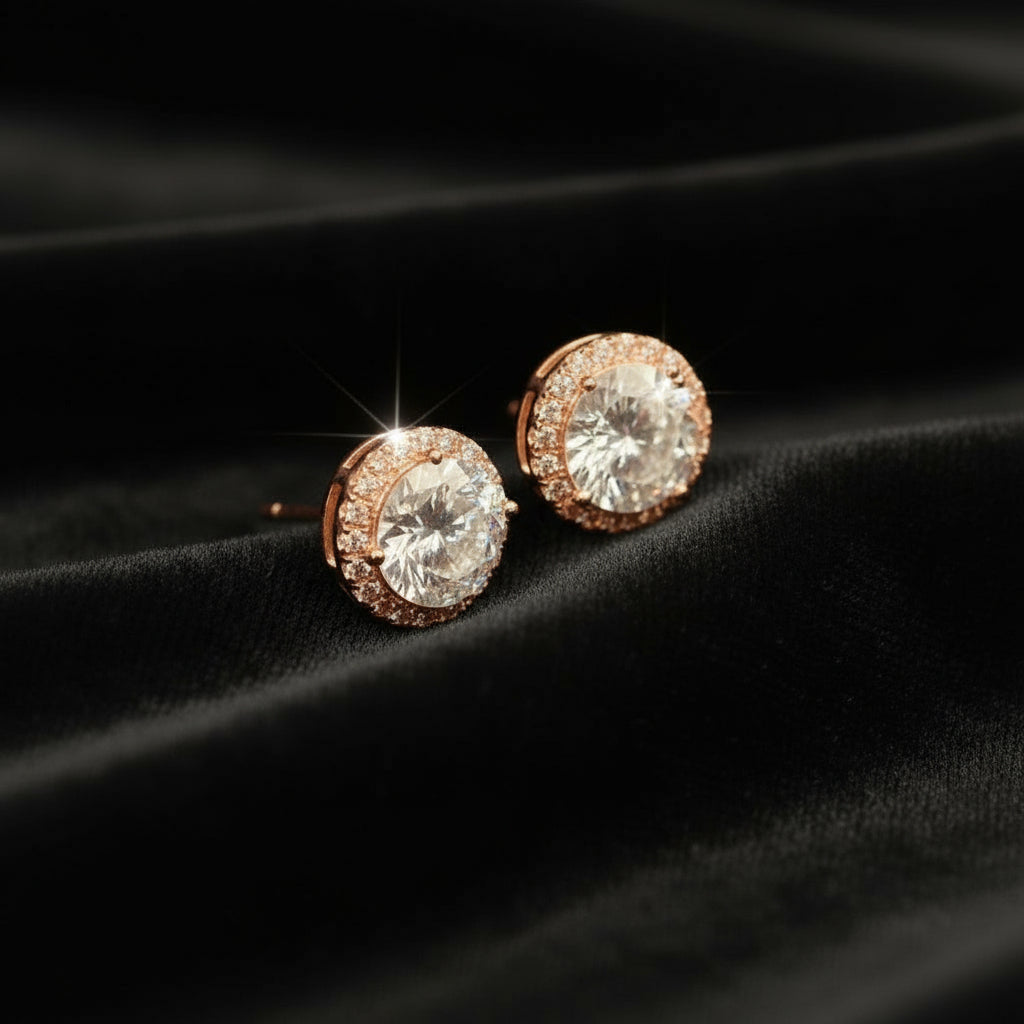 Rose gold earrings with clear gemstones on a black fabric background